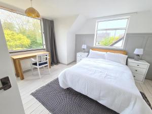 a white bedroom with a bed and a desk and two windows at Beach Chalet, Little Walsingham Norfolk in Little Walsingham