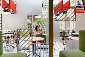a woman sitting at a table in a restaurant at MEININGER Hotel Bordeaux Gare Saint-Jean in Bordeaux