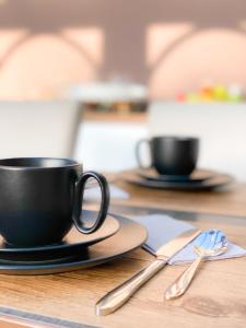two black coffee cups and spoons on a wooden table at B&B VILLA MONIQUE in Koksijde