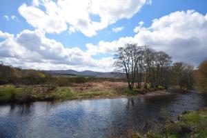 a river in a field with clouds in the sky at Feughside in Strachan