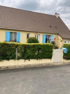 a yellow house with blue windows and a white fence at La Fossette in Asnelles