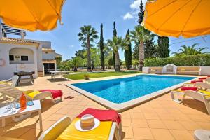 a pool with chairs and umbrellas in a backyard at Villa Candida by Villa Plus in Vale do Lobo