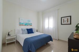 a white bedroom with a blue bed and a window at Living Las Canteras Homes - BEACHSIDE TERRACE BIKES in Las Palmas de Gran Canaria