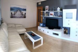 een woonkamer met een witte bank en een flatscreen-tv bij Beautiful apartment with swimming pool and beach in Alicante