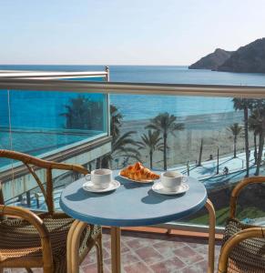 a table with a slice of pizza on a balcony with the ocean at KAKTUS Hotel Kaktus Albir in Albir
