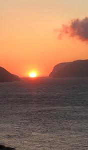 The Atlantic view guest house, Sandavagur, Faroe Islands في Sandavágur: غروب الشمس على المحيط مع الشمس في المسافة