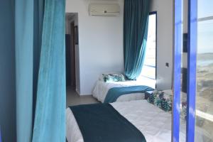 a bedroom with two beds with blue curtains and a window at Auberge Oualidia Dream in Oualidia