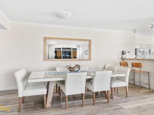 a dining room table with white chairs and a mirror at Breakwater Apartment 205 in Shoal Bay