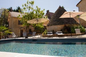 a swimming pool with chairs and umbrellas next to a house at Aux Bories de Marquay, B&B avec piscine et SPA près de Sarlat in Marquay
