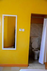 Baño amarillo con aseo y espejo en New Green Pastures Guest House, en Eldoret