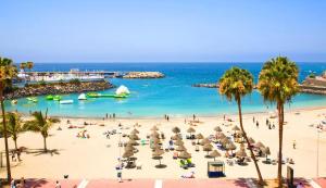 una spiaggia con persone e ombrelloni e l'oceano di El cortijo, pool view a Playa de las Americas