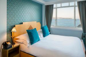 a bedroom with a bed with blue pillows and a window at Burgh Island Hotel in Bigbury on Sea