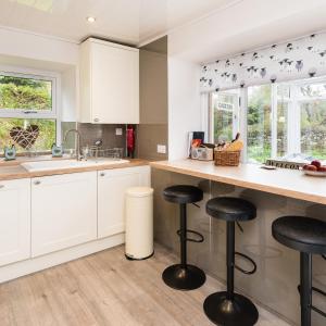 una cocina con armarios blancos y taburetes negros en Smithy Cottage en Kirkmichael