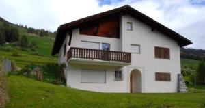 ein weißes Haus mit Balkon auf einem grünen Hügel in der Unterkunft Feriendomizil zum Schalten und Walten in Scuol