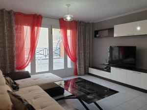 ein Wohnzimmer mit einem Sofa, einem TV und roten Vorhängen in der Unterkunft Penthouse Residencial Virginia in Torrevieja