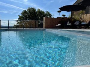 - une piscine d'eau bleue avec un parasol dans l'établissement Logis Au Vieux Morvan, à Château-Chinon