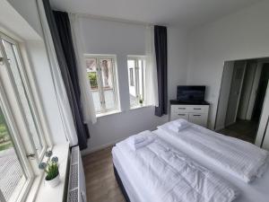a white bedroom with a bed and two windows at Nikolai Appartements in Rostock