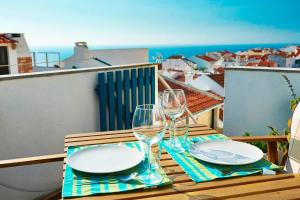 a table with two wine glasses and plates on a balcony at By the sea in the center @ Ericeira in Ericeira