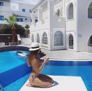 a woman in a hat sitting next to a swimming pool at Blue Suites in Fira