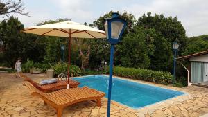 um guarda-sol e duas cadeiras ao lado de uma piscina em Pousada Recanto dos Encantos em Tiradentes