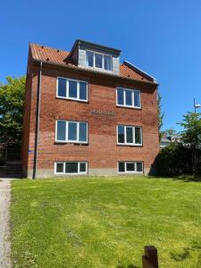 a red brick building with windows on a grass field at Hel lejlighed Thisted Midtby in Thisted