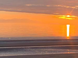a beach at sunset with the sun setting over the ocean at Ayr Cozy Corner Apartment in Ayr