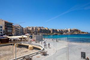 um grupo de pessoas caminhando em uma praia perto da água em Electra Residence - Luxury Central Beachview Apartment em Marsalforn