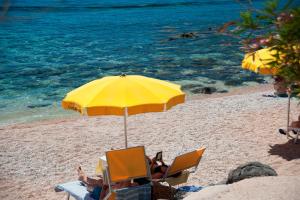 two people sitting in chairs under an umbrella on a beach at Costa Dorada in Cala Gonone