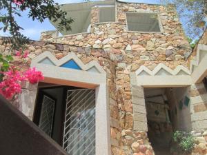 a stone building with two windows and pink flowers at Sardinia Yellow House in Solanas