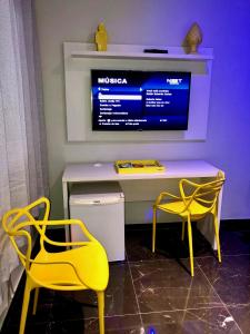 two yellow chairs and a desk with a television at Motel Del Fuego (Adult Only) in Pelotas