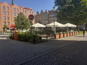 una calle con mesas, sombrillas blancas y edificios en KWATERA en Gdansk