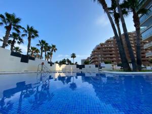 a swimming pool with palm trees and a building at Las Terrazas I - Primera línea de playa con Netflix, Disney plus y Prime Video in Oropesa del Mar