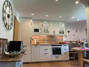 a kitchen with white cabinets and a clock on the wall at Landhaus Gastager in Ruhpolding