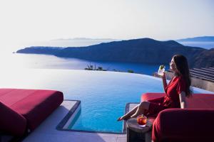 a woman in a red dress sitting next to a swimming pool at White Pearl Cavalieri in Imerovigli