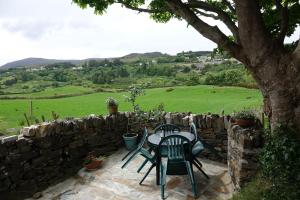 a patio with a table and chairs and a stone wall at Bell Cottage in Gortahork