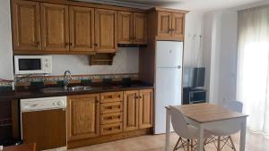cocina con armarios de madera, mesa y nevera blanca en Apartamentos Balcon de Carabeo, en Nerja