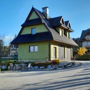 a house with a gambrel roof with a table and chairs at Tu i Teraz - domek in Bukowina Tatrzańska