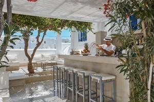 a man in a hat standing at a bar in a restaurant at Kouros Village Hotel - Adults Only in Perissa