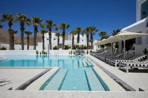 a swimming pool with chairs and palm trees at Kouros Village Hotel - Adults Only in Perissa