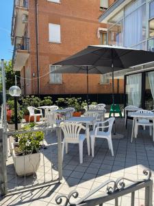 un patio con tavoli e sedie bianchi e ombrellone di Hotel Orlov Rimini a Rimini