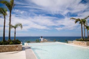 a woman standing next to a swimming pool next to the ocean at Empire Beach Resort ADULTS ONLY in Dhërmi