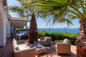 d'une terrasse avec des chaises, une table et des palmiers. dans l'établissement Splendida Villa con vista mozzafiato e piscina, à Terrasini