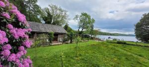 a house on the shore of a lake with purple flowers at Loch Lomond shore Boat House in Balmaha