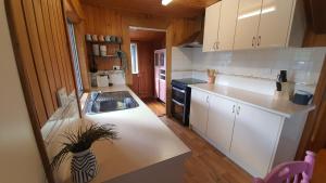 uma cozinha com armários brancos e um lavatório em Cottage on Herbert em Ravenshoe
