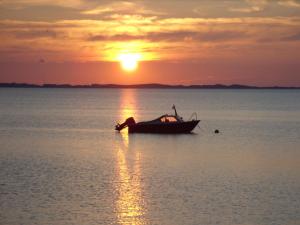 a boat sitting in the water at sunset at Ferienwohnungen im Hotel garni zur Post in Utersum +6 photos