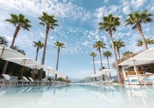 una piscina con palmeras, sillas y sombrillas en Nikki Beach Resort & Spa Montenegro en Tivat