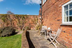 a patio with chairs and a table and a brick building at Chirk Cottage at Hill House Farm Cheshire in Tarporley