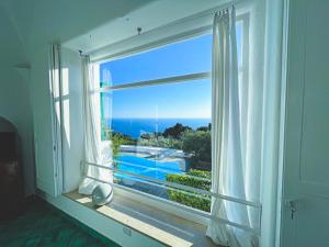 a window with a view of a pool and the ocean at Il Carrubo Capri in Anacapri