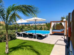 a backyard with a swimming pool with chairs and an umbrella at Villa Izabela in Hersonissos