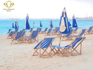 a group of blue chairs and umbrellas on a beach at Jewel Matrouh Hotel in Marsa Matruh